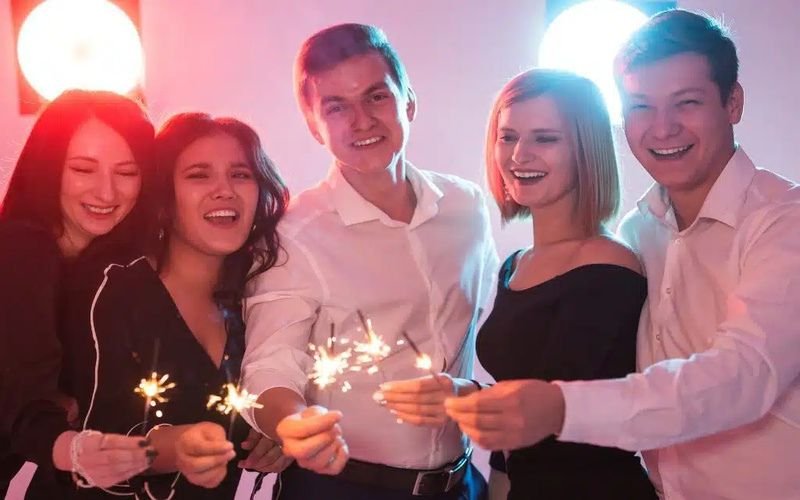 A group of adults celebrating a birthday party, holding sparklers and smiling under colorful lighting. Perfect example of birthday party entertainment for adults.