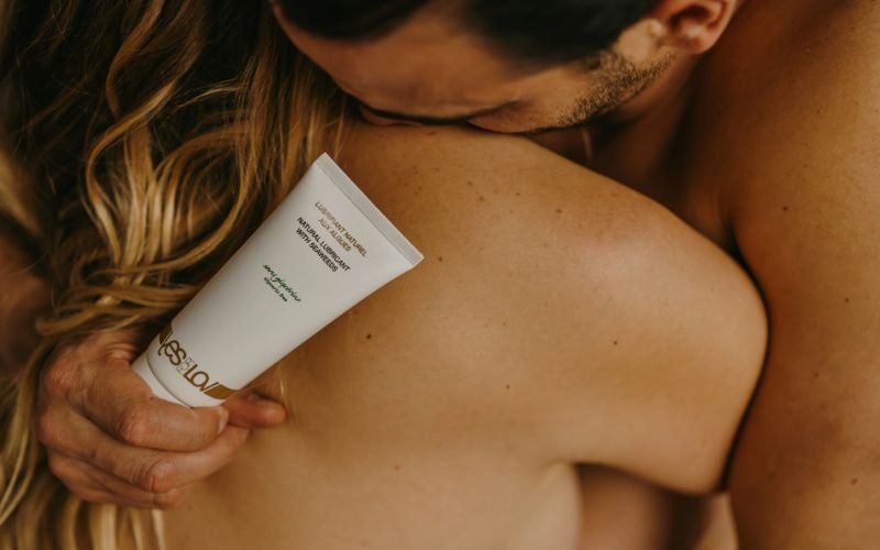 A couple embracing intimately while holding a tube of lubricant, emphasizing sensual connection and preparation.