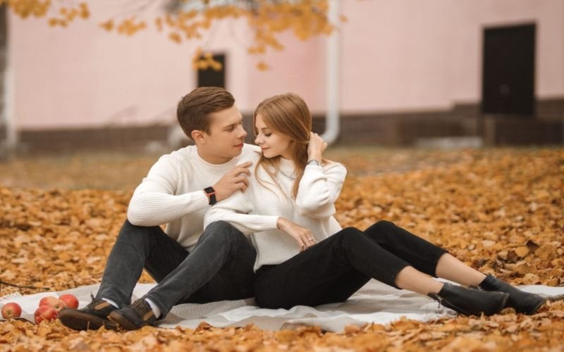 A couple sitting on a blanket in an autumn park, surrounded by fallen leaves, symbolizing romantic moments on European adult dating websites.