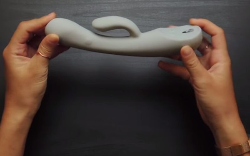 Close-up of hands holding a modern grey vibrator with ergonomic design, one of the best woman sex toys.